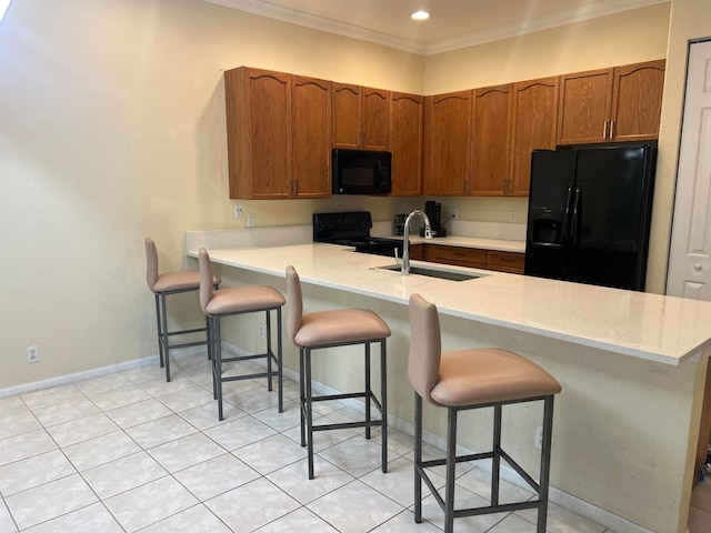 kitchen featuring ornamental molding, light tile patterned floors, sink, a breakfast bar area, and black appliances