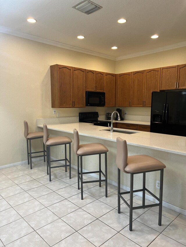 kitchen featuring sink, crown molding, black appliances, a breakfast bar area, and light tile patterned flooring