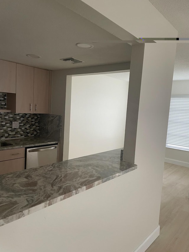 kitchen featuring tasteful backsplash, stainless steel dishwasher, light hardwood / wood-style floors, and light stone counters