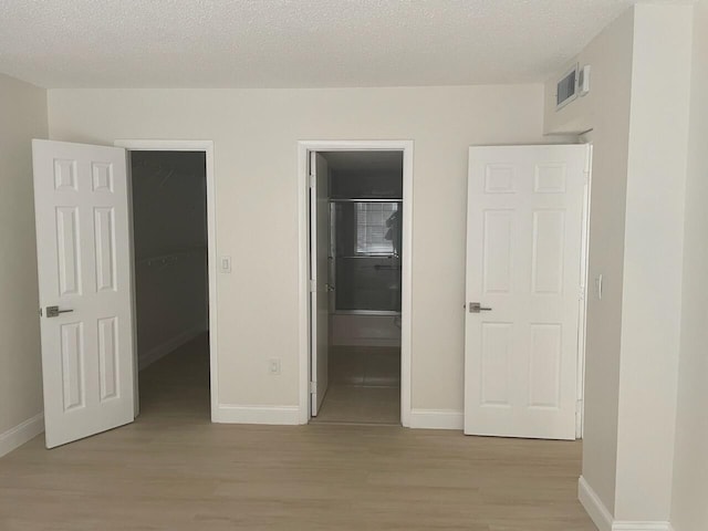 unfurnished bedroom featuring a walk in closet, light hardwood / wood-style flooring, a textured ceiling, and ensuite bath