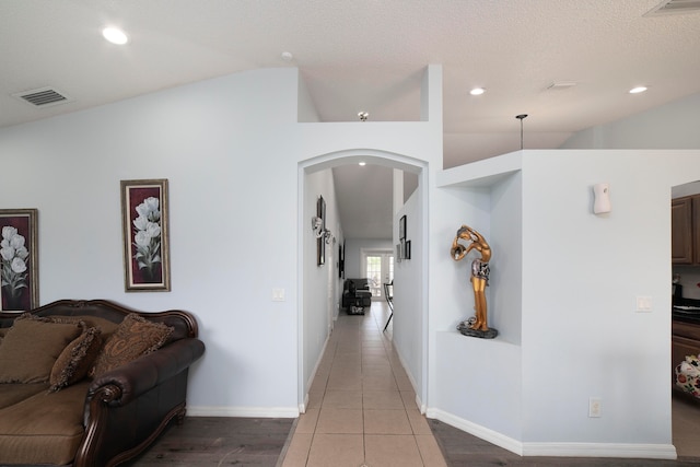 hall featuring a textured ceiling, lofted ceiling, and tile patterned floors