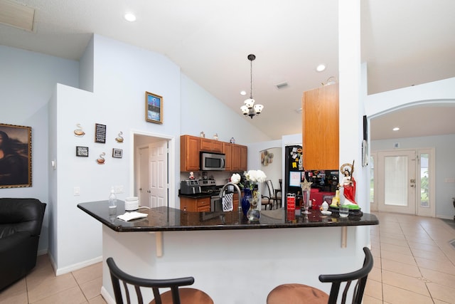 kitchen featuring light tile patterned flooring, dark stone counters, hanging light fixtures, appliances with stainless steel finishes, and kitchen peninsula