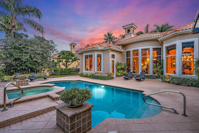 pool at dusk with an in ground hot tub and a patio