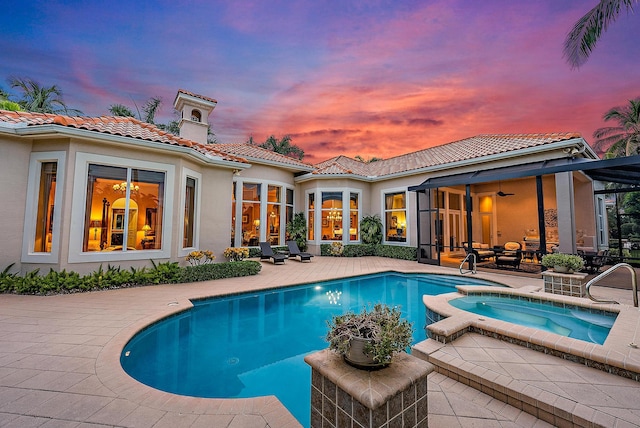 pool at dusk with a patio area and an in ground hot tub