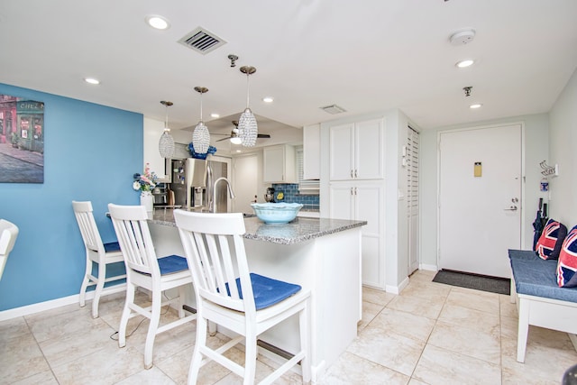 kitchen featuring tasteful backsplash, light stone counters, white cabinets, stainless steel fridge with ice dispenser, and light tile patterned flooring