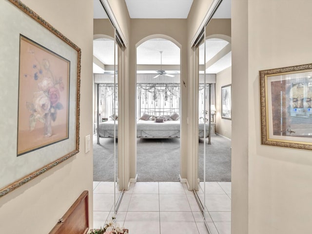 hall with light tile patterned flooring, baseboards, arched walkways, and light carpet