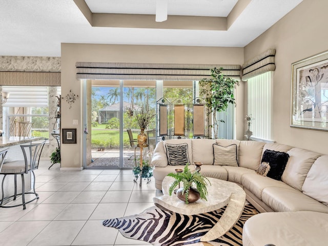 living area with light tile patterned floors, baseboards, and a raised ceiling