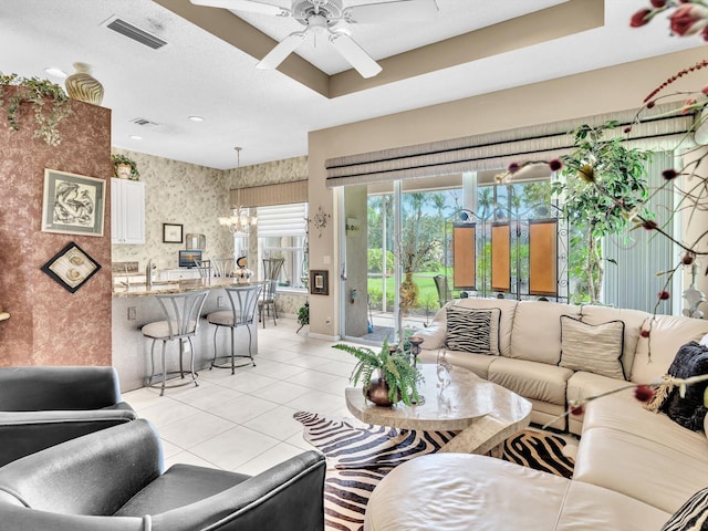 living area featuring visible vents, wallpapered walls, ceiling fan with notable chandelier, light tile patterned flooring, and a raised ceiling