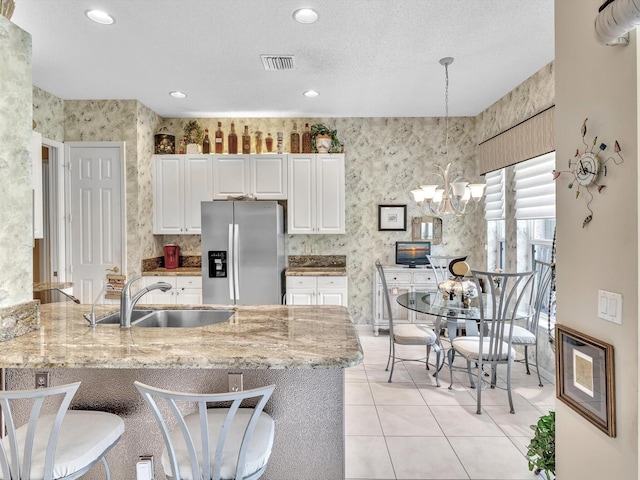 kitchen with visible vents, wallpapered walls, stainless steel fridge with ice dispenser, a sink, and white cabinets