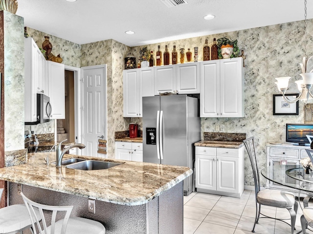 kitchen with wallpapered walls, a peninsula, a sink, black microwave, and stainless steel fridge