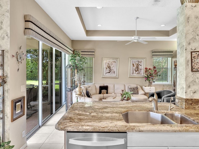 kitchen featuring stainless steel dishwasher, a tray ceiling, light stone counters, and a sink