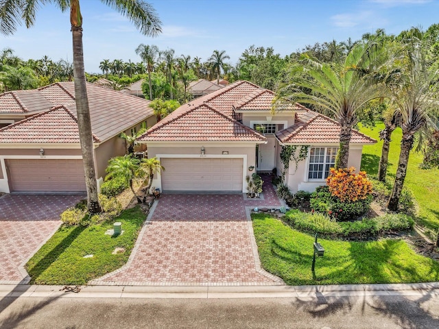 mediterranean / spanish house featuring a tiled roof, stucco siding, an attached garage, and decorative driveway