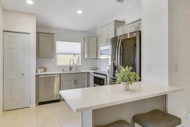 kitchen featuring a peninsula, appliances with stainless steel finishes, a sink, and gray cabinetry