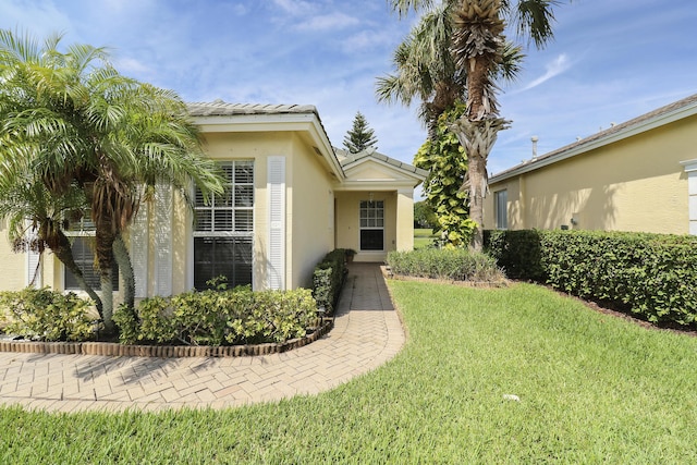 doorway to property with a tile roof, a lawn, and stucco siding