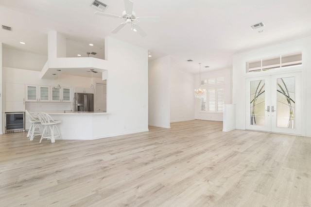 unfurnished living room featuring french doors, wine cooler, light wood-type flooring, and ceiling fan with notable chandelier