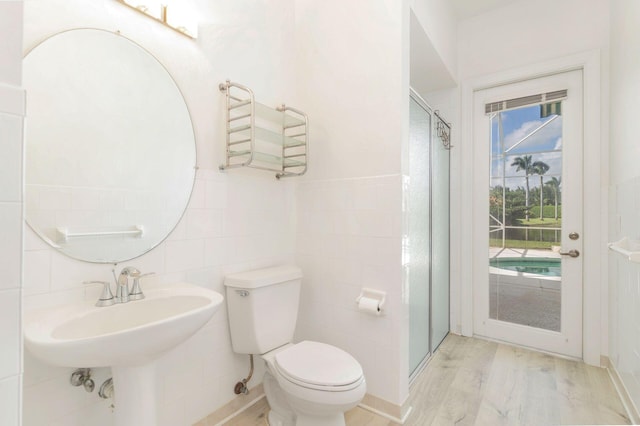 bathroom with a shower with door, hardwood / wood-style flooring, toilet, and tile walls