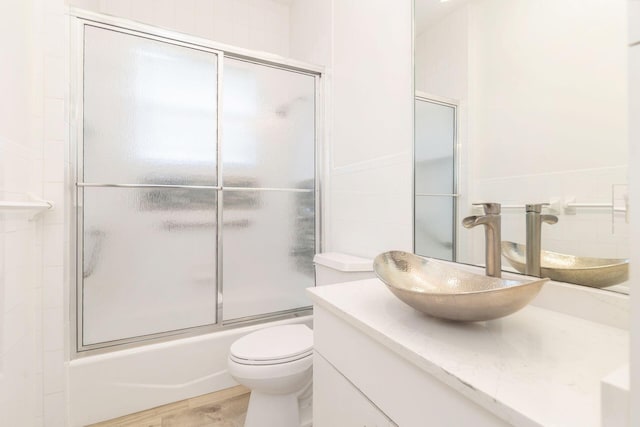 full bathroom featuring vanity, toilet, wood-type flooring, and bath / shower combo with glass door