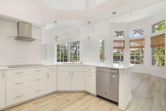 kitchen with stainless steel dishwasher, hanging light fixtures, wall chimney range hood, and a wealth of natural light