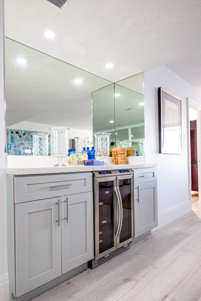 bar with gray cabinets, beverage cooler, and light hardwood / wood-style floors