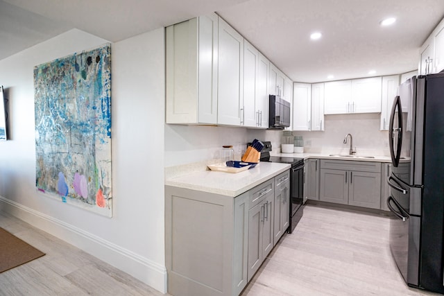 kitchen with black range with electric stovetop, sink, stainless steel refrigerator, gray cabinets, and light wood-type flooring