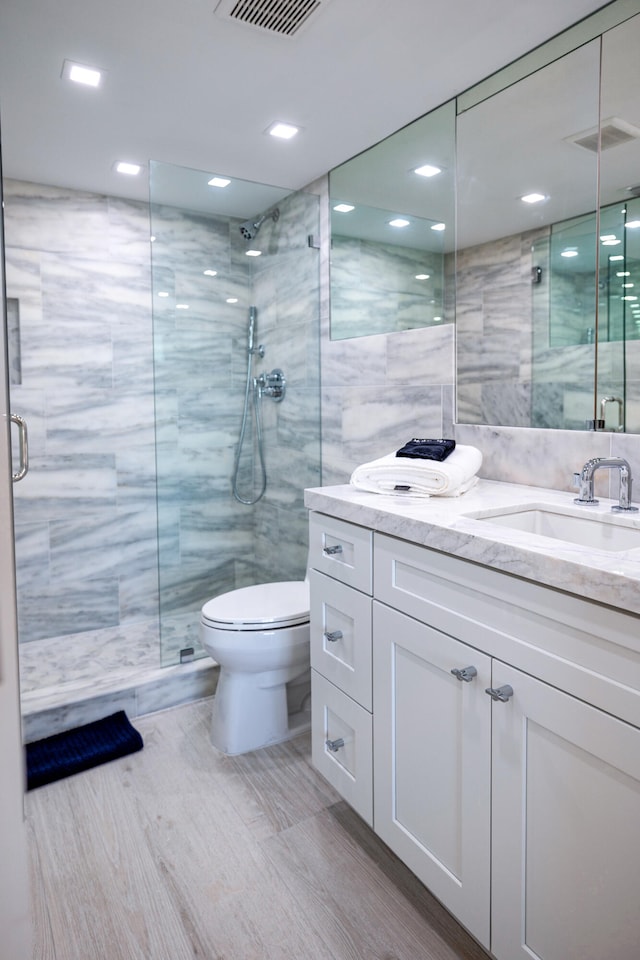 bathroom with tile walls, a shower with shower door, vanity, and toilet