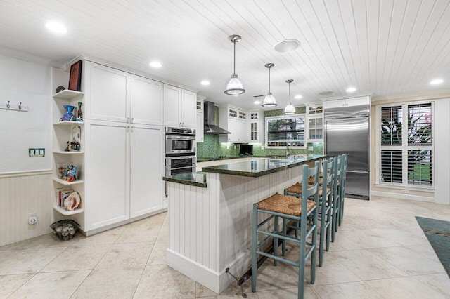 kitchen featuring a center island, appliances with stainless steel finishes, a breakfast bar area, white cabinets, and wall chimney range hood