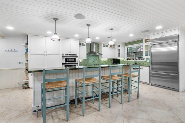 kitchen featuring white cabinetry, a center island, hanging light fixtures, wall chimney exhaust hood, and appliances with stainless steel finishes