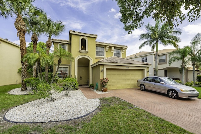 mediterranean / spanish home featuring decorative driveway, a tile roof, stucco siding, an attached garage, and a front lawn