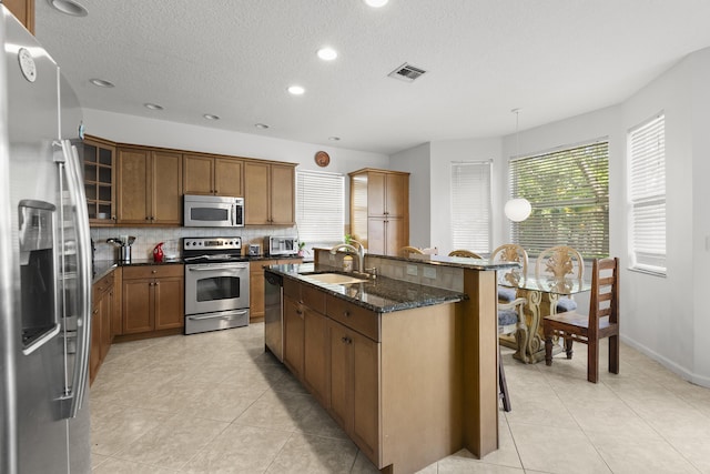 kitchen featuring stainless steel appliances, brown cabinetry, a sink, and visible vents