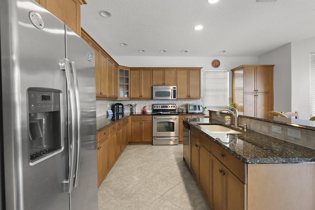 kitchen with tasteful backsplash, appliances with stainless steel finishes, brown cabinetry, glass insert cabinets, and a sink