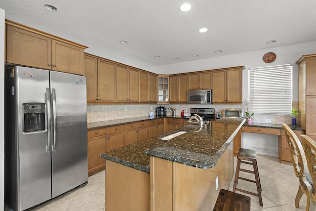 kitchen with brown cabinets, stainless steel appliances, glass insert cabinets, a sink, and an island with sink