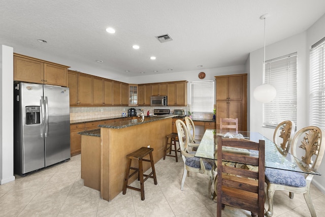 kitchen featuring stainless steel appliances, dark stone countertops, visible vents, and brown cabinets