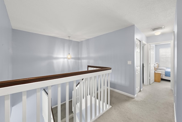 corridor with baseboards, visible vents, light colored carpet, a textured ceiling, and an upstairs landing