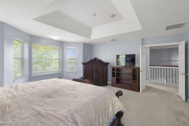 bedroom with a textured ceiling, a tray ceiling, visible vents, and light colored carpet