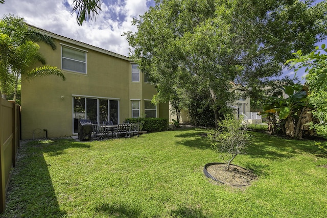 back of house featuring a lawn, fence, and stucco siding