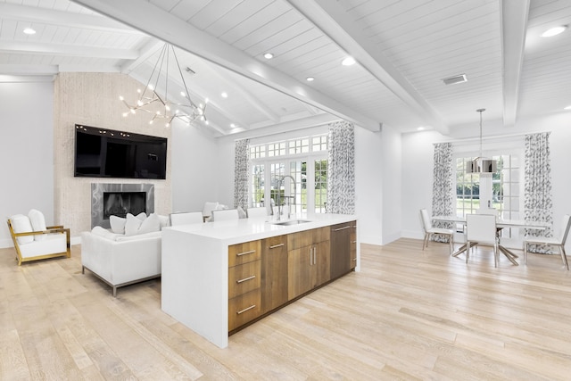 kitchen featuring pendant lighting, light wood-type flooring, a fireplace, vaulted ceiling with beams, and a center island with sink