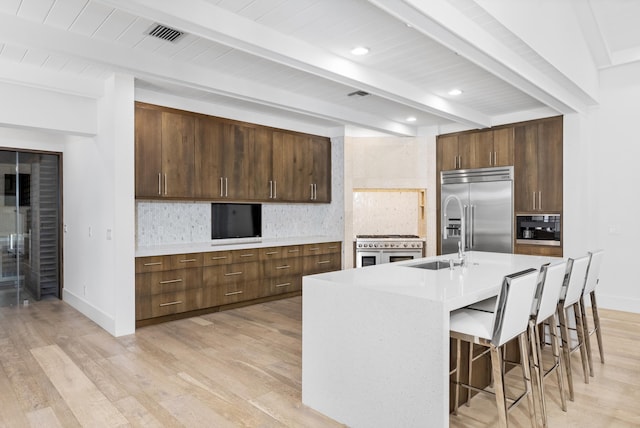 kitchen with a breakfast bar, light wood-type flooring, a kitchen island with sink, tasteful backsplash, and high quality appliances