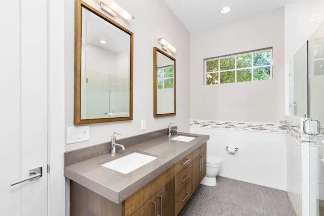 bathroom with tile walls, a shower with shower door, vanity, toilet, and tile patterned floors