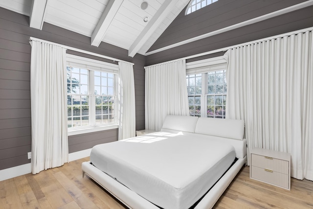 bedroom with light wood-type flooring, vaulted ceiling with beams, wood walls, and multiple windows