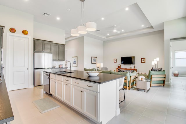 kitchen featuring stainless steel dishwasher, a tray ceiling, a kitchen island with sink, sink, and light tile patterned floors