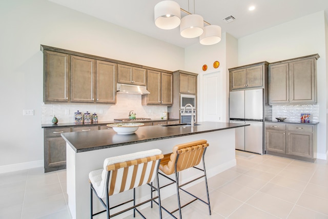 kitchen with sink, an island with sink, hanging light fixtures, and fridge