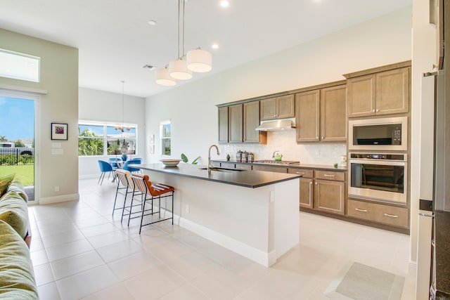 kitchen with sink, hanging light fixtures, stainless steel appliances, a kitchen island with sink, and light tile patterned floors