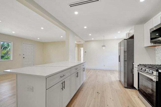 kitchen featuring light wood-type flooring, appliances with stainless steel finishes, light stone counters, white cabinetry, and a kitchen island