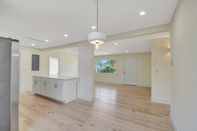 interior space featuring a barn door, decorative light fixtures, electric panel, light hardwood / wood-style floors, and white cabinetry