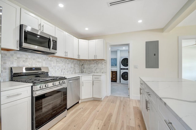 kitchen featuring light wood-type flooring, appliances with stainless steel finishes, electric panel, stacked washer and clothes dryer, and sink