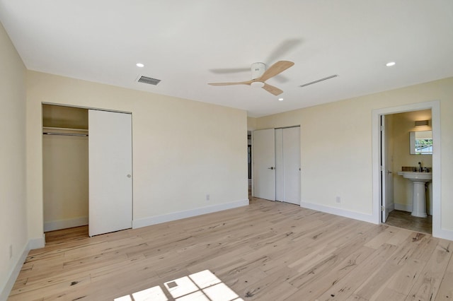 unfurnished bedroom featuring ceiling fan, light hardwood / wood-style floors, multiple closets, and ensuite bath