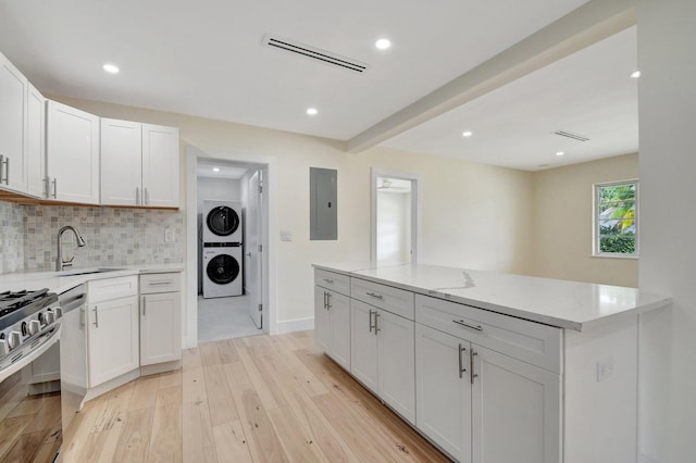 kitchen with stacked washer and clothes dryer, tasteful backsplash, stainless steel appliances, sink, and electric panel