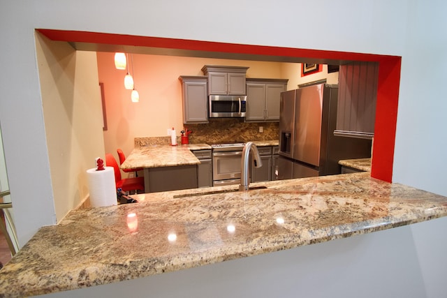 kitchen with backsplash, light stone counters, kitchen peninsula, stainless steel appliances, and gray cabinets