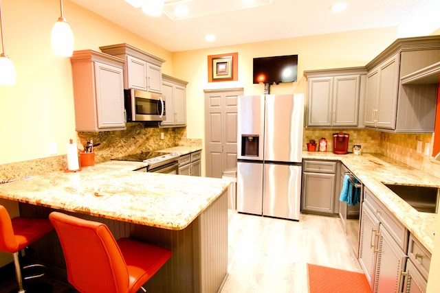 kitchen with appliances with stainless steel finishes, decorative backsplash, a kitchen bar, light wood-type flooring, and kitchen peninsula