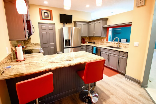 kitchen featuring a kitchen breakfast bar, appliances with stainless steel finishes, light hardwood / wood-style flooring, and backsplash